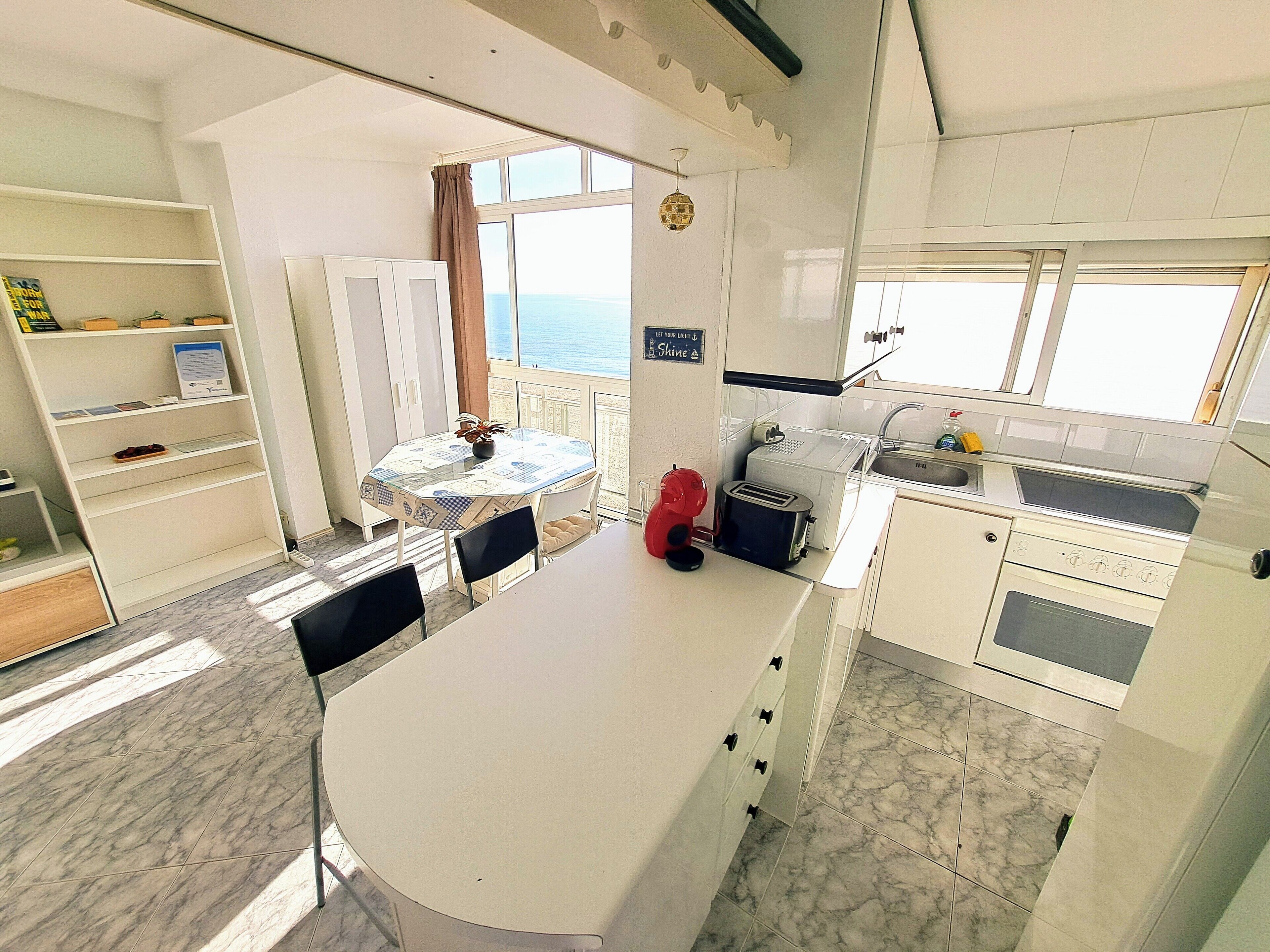 Een kleine keuken met een eethoek, uitzicht op zee en een tafeltje met stoelen.
