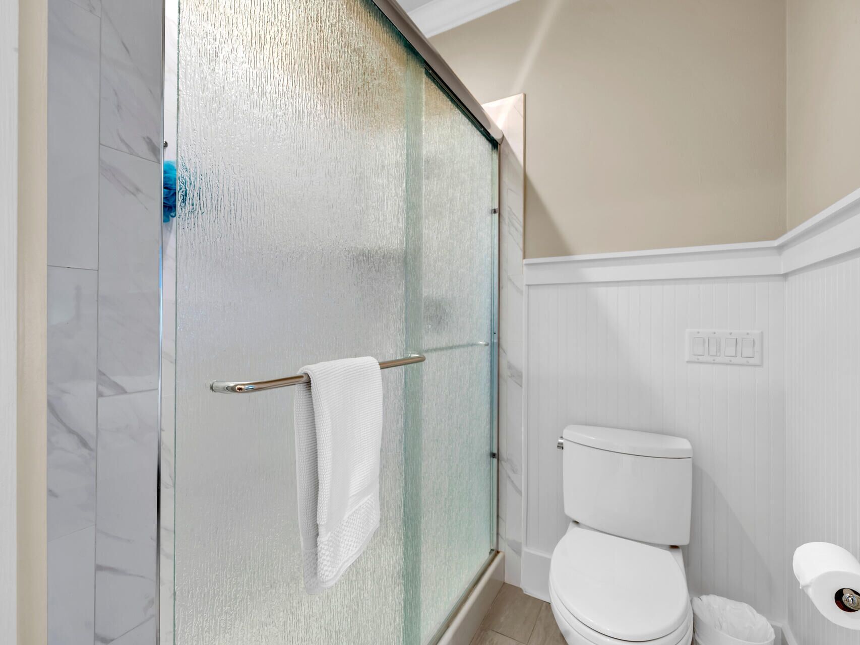 A bathroom with a glass shower door, a white toilet, and a towel rack.
