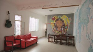 Una sala de estar con un sofá rojo, una mesa de comedor con sillas, una guitarra y un mural grande en la pared.