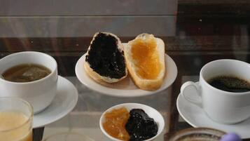 A table with a glass of tea, a cup of coffee, and two small bowls with jam.