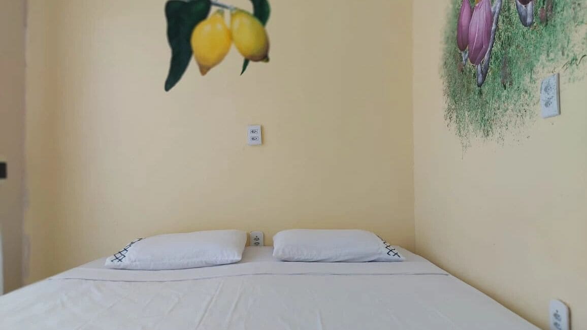 Un dormitorio con cama, dos almohadas, un interruptor de luz en la pared y una decoración de limones en la pared.