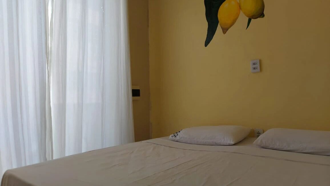 Une pièce avec un lit, des rideaux blancs et un interrupteur fixé au mur.