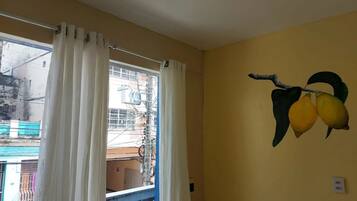 Una habitación con un ventanal grande, cortinas blancas y un mural en la pared con dos limones.