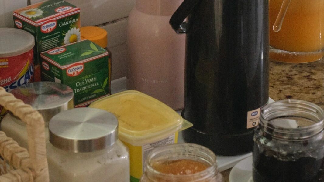 En køkkenbordplade med forskellige madvarer og beholdere, herunder en kaffemaskine, krukker og æsker med Dr. Oetker produkter.