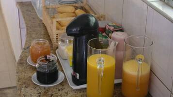 Una encimera de cocina con diversos alimentos y bebidas, incluyendo frascos de conservas, una cafetera y vasos de zumo de naranja.