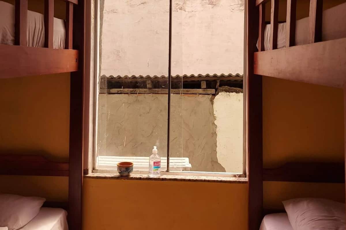 Quarto com beliche, uma janela, uma garrafa de água e uma caneca no parapeito.