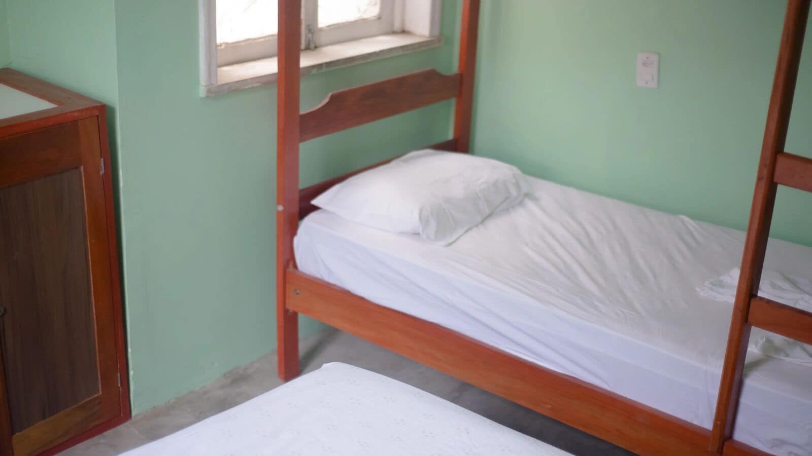 A simple bunk bed room with a wooden frame, white bedding, and a window above the bed.