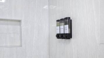 Un distributeur mural doté de trois compartiments étiquetés « SHAMPOO », « APRÈS-SHAMPOO » et « GEL DOUCHE ».