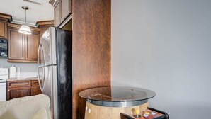 Une cuisine dotée de meubles en bois, d’un réfrigérateur en acier inoxydable et d’une table basse originale en forme de tonneau, également en bois, surmontée d’un plateau en verre.