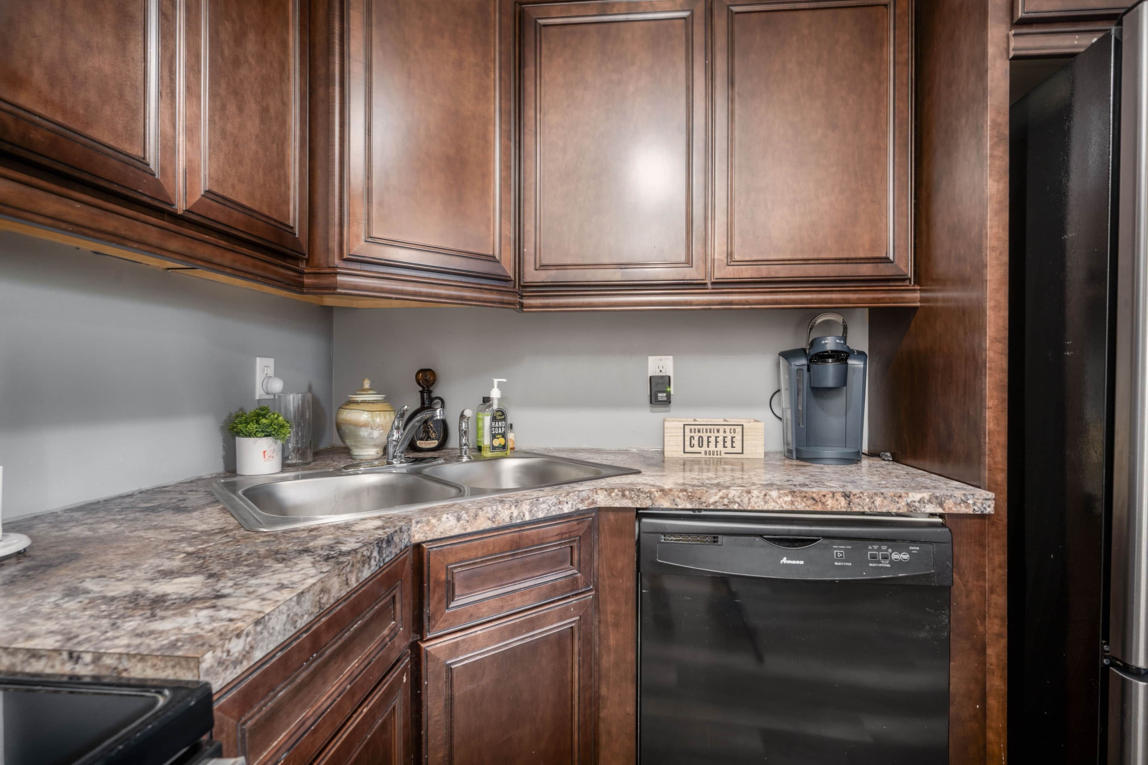 A kitchen with wooden cabinets, a granite countertop, a coffee maker, and a dishwasher.