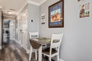 A dining area with a table and chairs, a framed poster on the wall, and a door leading to another room.