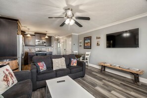 A modern living room with a black sofa, a white coffee table, and a ceiling fan.
