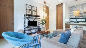 A modern living room with a sofa, a blue chair, a TV, and a kitchen area with a microwave. - Manor Tulum (Tulum)