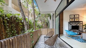 A balcony with a bamboo fence, wicker chairs, a small table, and a TV on a stand. - Manor Tulum (Tulum)