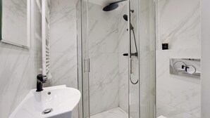 Une salle de bain moderne avec une douche à parois de verre, un lavabo blanc et des murs en marbre.