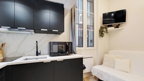 Une cuisine compacte équipée d’un four à micro-ondes, de meubles noirs, d’un plan de travail blanc et d’un canapé blanc dans le salon attenant.