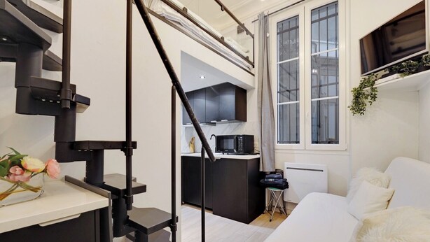 Un espace de vie compact comprenant un coin cuisine, un lit avec des oreillers moelleux et un escalier menant à un niveau supérieur.