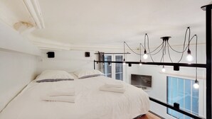 Une chambre moderne avec un grand lit, une télévision et une vue sur la ville grâce à de grandes fenêtres.