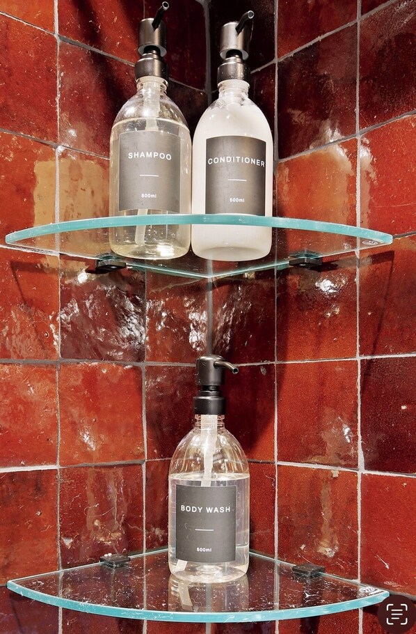 Une salle de bain avec trois étagères en verre sur lesquelles sont posées des bouteilles de shampoing, d’après-shampoing et de gel douche.