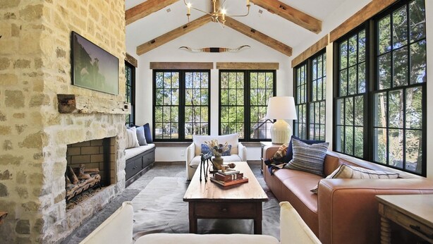 Una sala de estar acogedora con chimenea de piedra, vigas de madera, ventanas amplias y asientos cómodos.