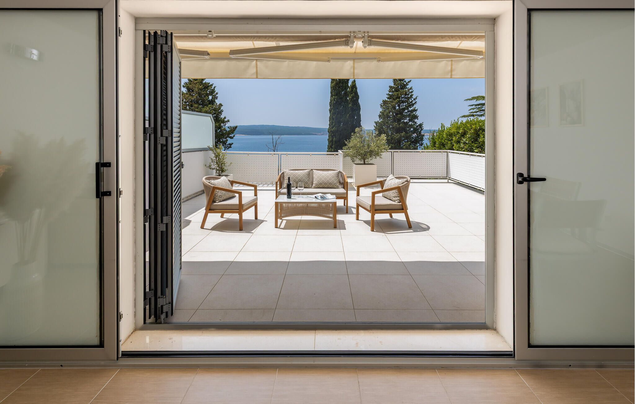 Une porte coulissante s’ouvre sur un patio aménagé avec du mobilier d’extérieur et offrant une vue sur la mer.