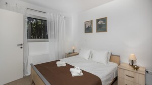 Una camera d'albergo con un letto, un comodino con una lampada, una piccola cassettiera e due quadri appesi al muro.
