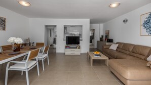 Un soggiorno moderno con un divano in pelle marrone, una zona pranzo con tavolo in legno e sedie bianche, un mobile TV con televisore a schermo piatto e angolo cottura con pensili e forno a microonde.