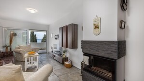 Uma sala de estar moderna com lareira, sofá, televisão e vista para o exterior.