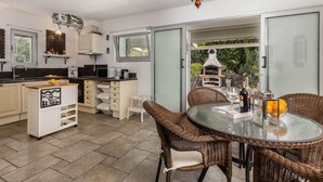 Cozinha moderna com área de refeições, destacando uma mesa de vidro, cadeiras de vime e um forno a pizza.