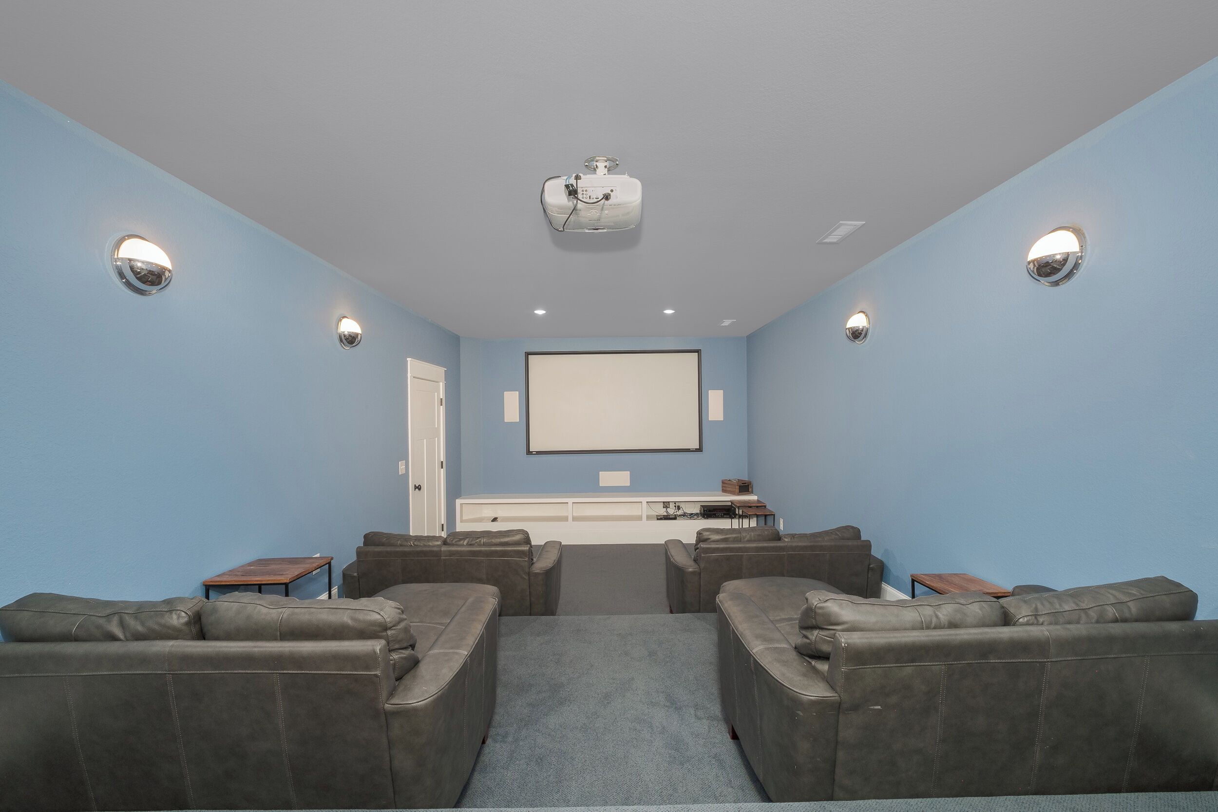 A home theater room with a large screen, ceiling-mounted projector, and leather couches.