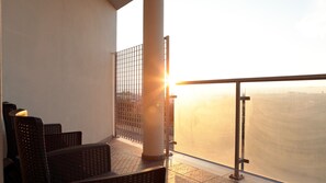 A balcony with a view of the cityscape during sunset, featuring a railing and seating area.