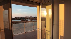 A view from a balcony with a glass door, overlooking a body of water and trees.