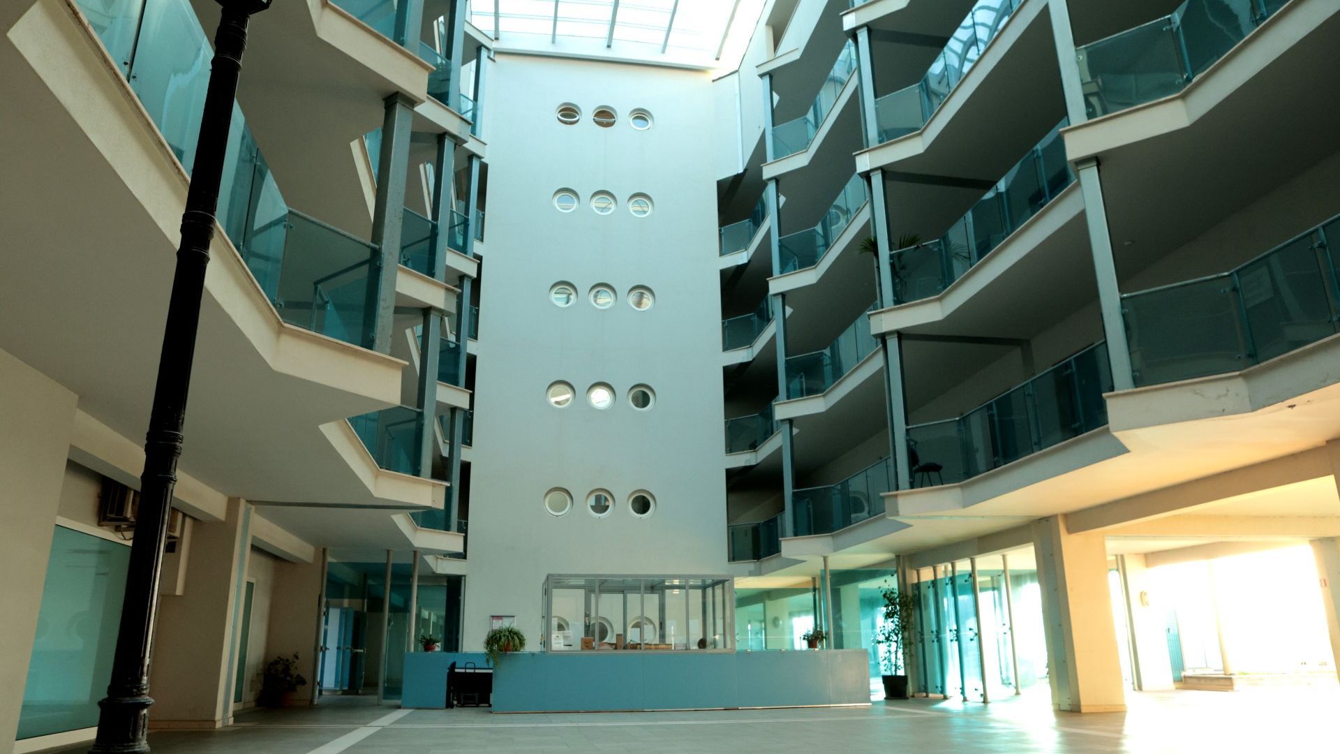 Un interior moderno con un atrio central, varios balcones y un mostrador de recepción.