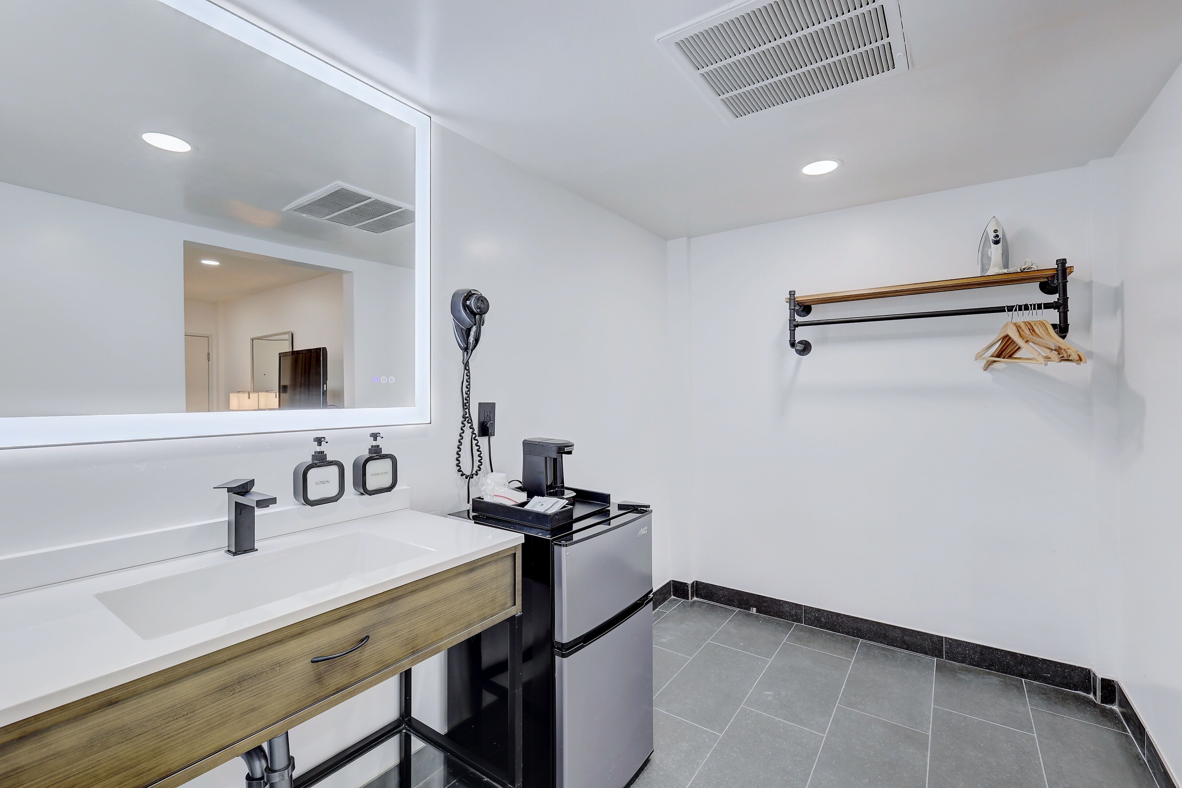 Une salle de bain moderne avec un meuble-lavabo blanc, un miroir, un sèche-cheveux et un petit réfrigérateur.