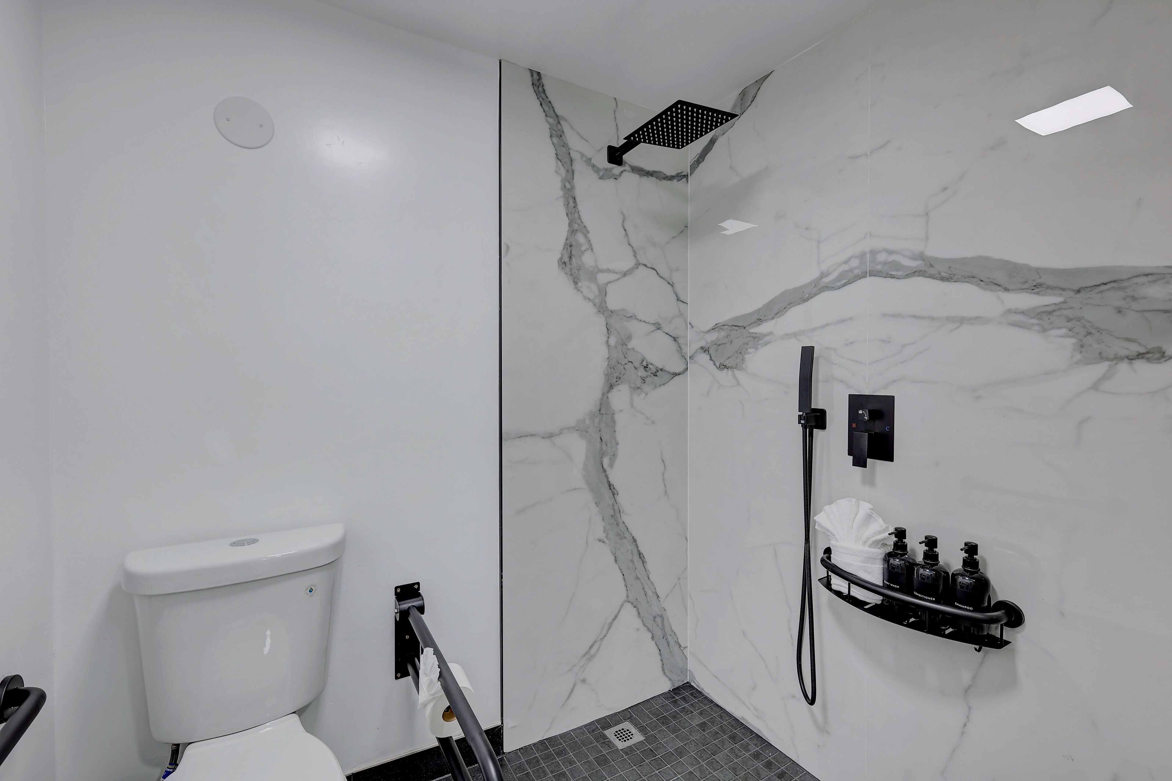 A modern bathroom with a toilet, a shower with a glass door, and a shelf with toiletries.