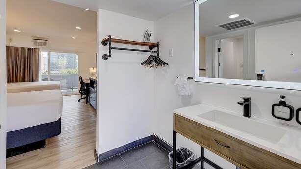 A modern hotel room with a large mirror, a wooden vanity, and a bed with a view of the city. - Ash&9th (San Diego)