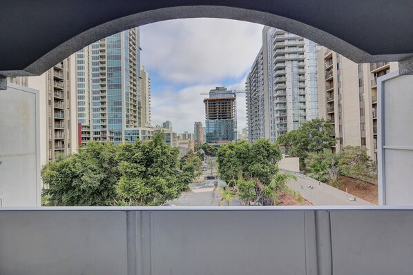 A view through an arched window of a residential area with tall buildings, trees, and a construction site in the distance.
