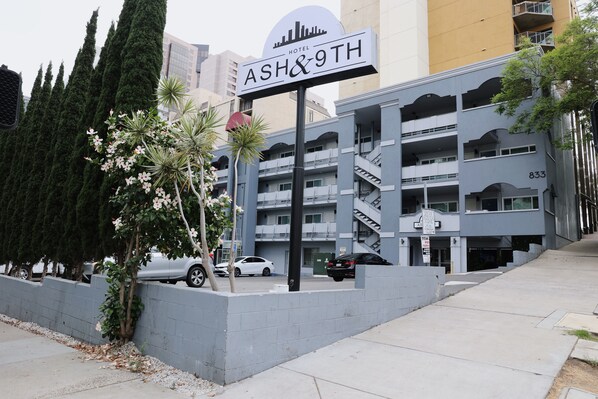 Ein Schild des Hotels "ASH&9TH" mit einem modernen Gebäude im Hintergrund.
