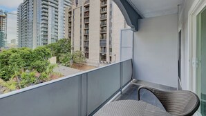 A balcony with a wicker chair, a view of high-rise buildings, and a small garden area. - Ash&9th (San Diego)