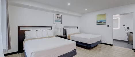 Una habitación de hotel con dos camas individuales, un ventanal grande y un baño visible al fondo.