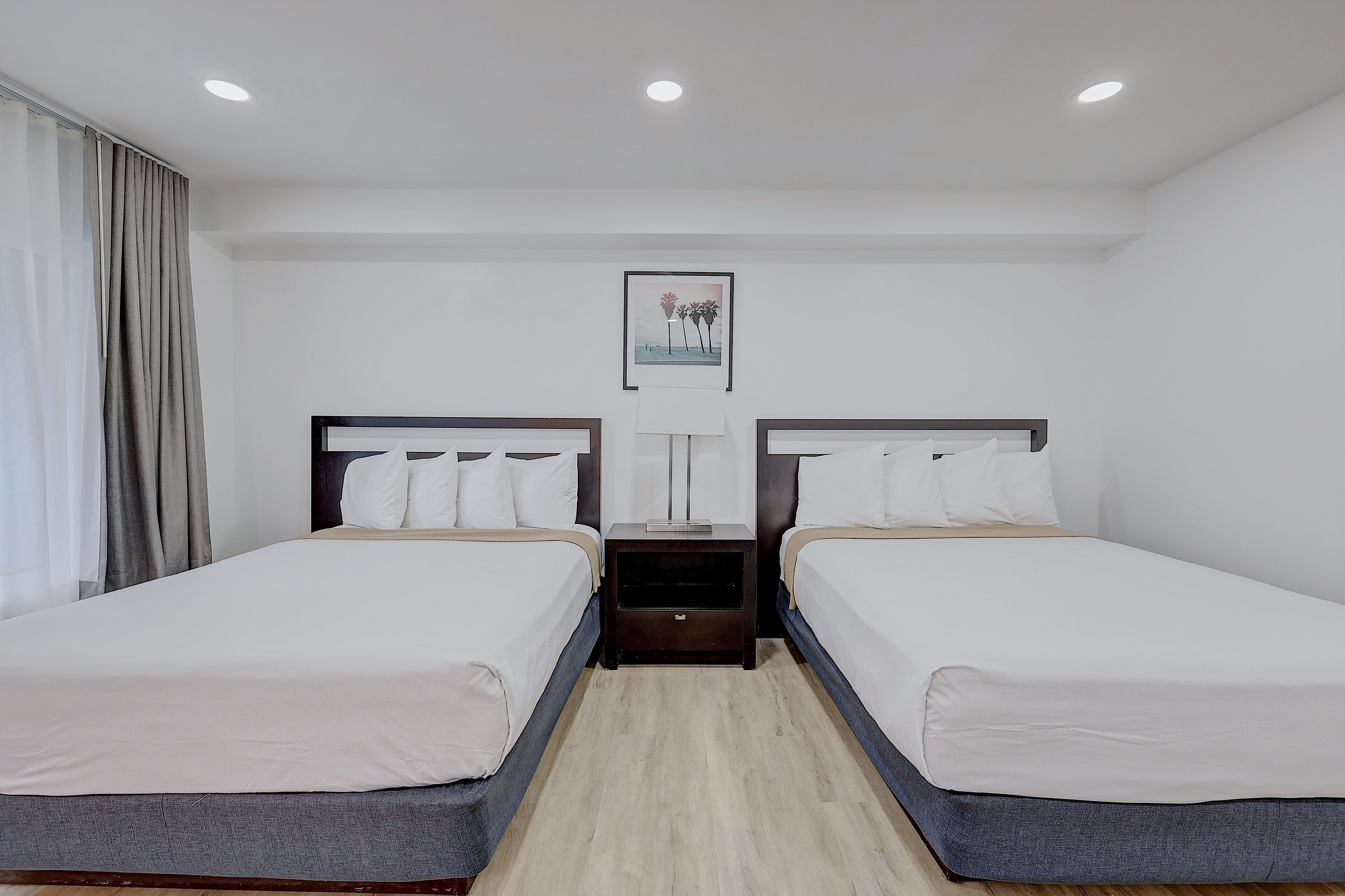 A hotel room with two single beds, a nightstand between them, a lamp, and a framed picture on the wall.