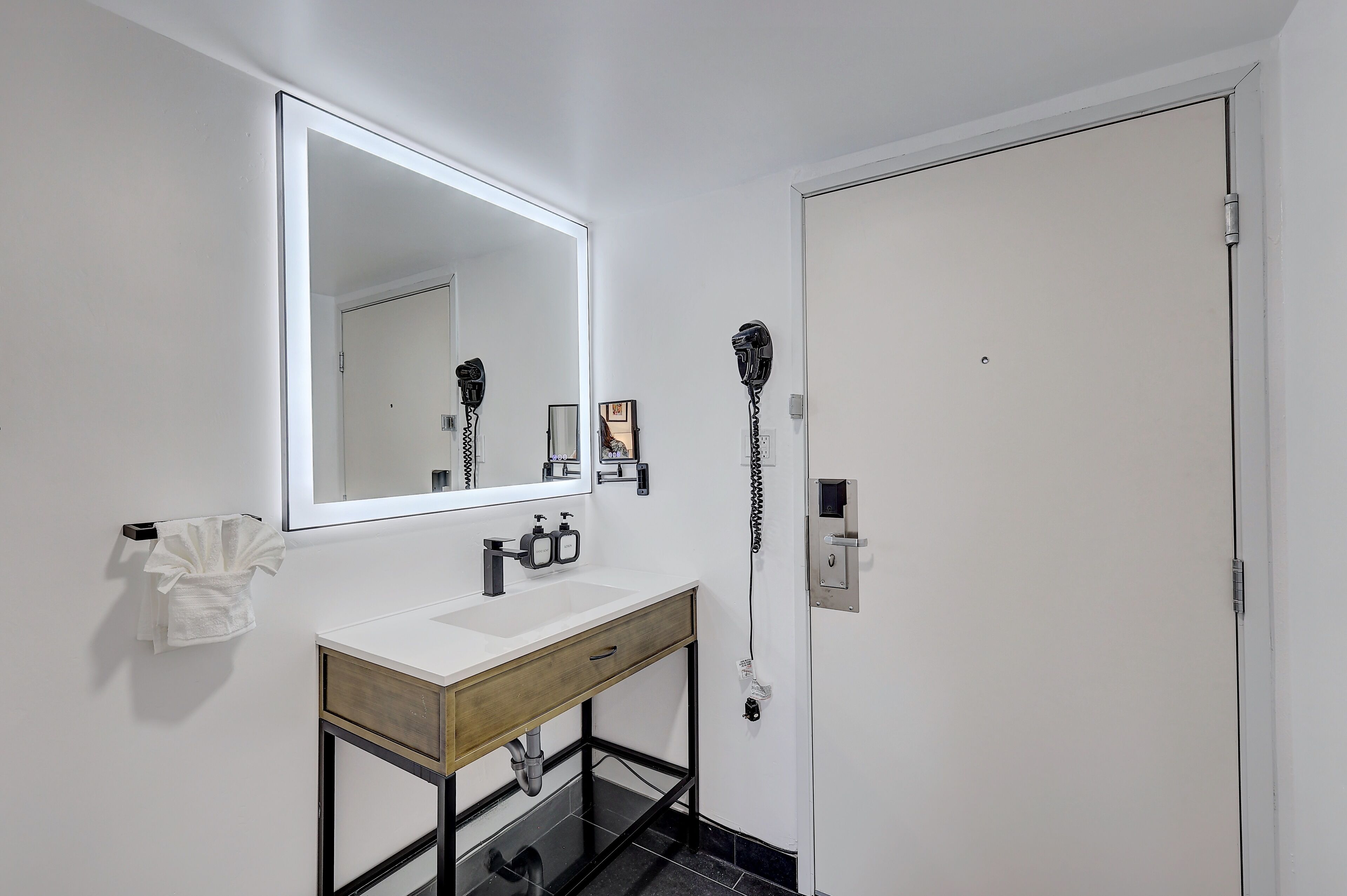 A modern bathroom with a white vanity, a large mirror, and a hairdryer mounted on the wall.