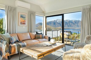 A modern living room with a sofa, coffee table, and a view of mountains and a lake. - Ski Chalet Vibe - Stunning Lake & Mountain Views! (Queenstown)