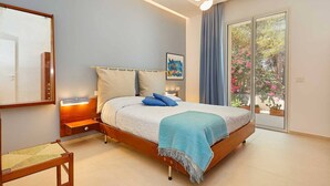 Un dormitorio con cama, mesitas de noche, una silla, un ventanal con vistas a plantas y un ventilador de techo.