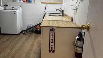 Una pequeña kitchenette con encimera de madera, un extintor y una lavadora al fondo.