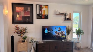 Un salon moderne avec un téléviseur à écran plat, des œuvres d’art encadrées, une étagère décorative et une plante en pot.