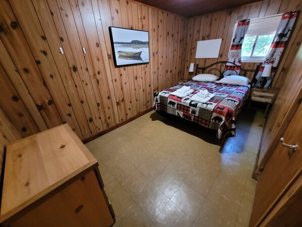 A wooden-paneled room with a bed, a desk, and a window with curtains.