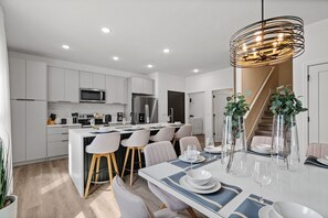 A modern kitchen with white cabinets, a central island, and a dining area with a white table and chairs. - Stylish Getaway 15 Min From Disney Parks (Davenport)
