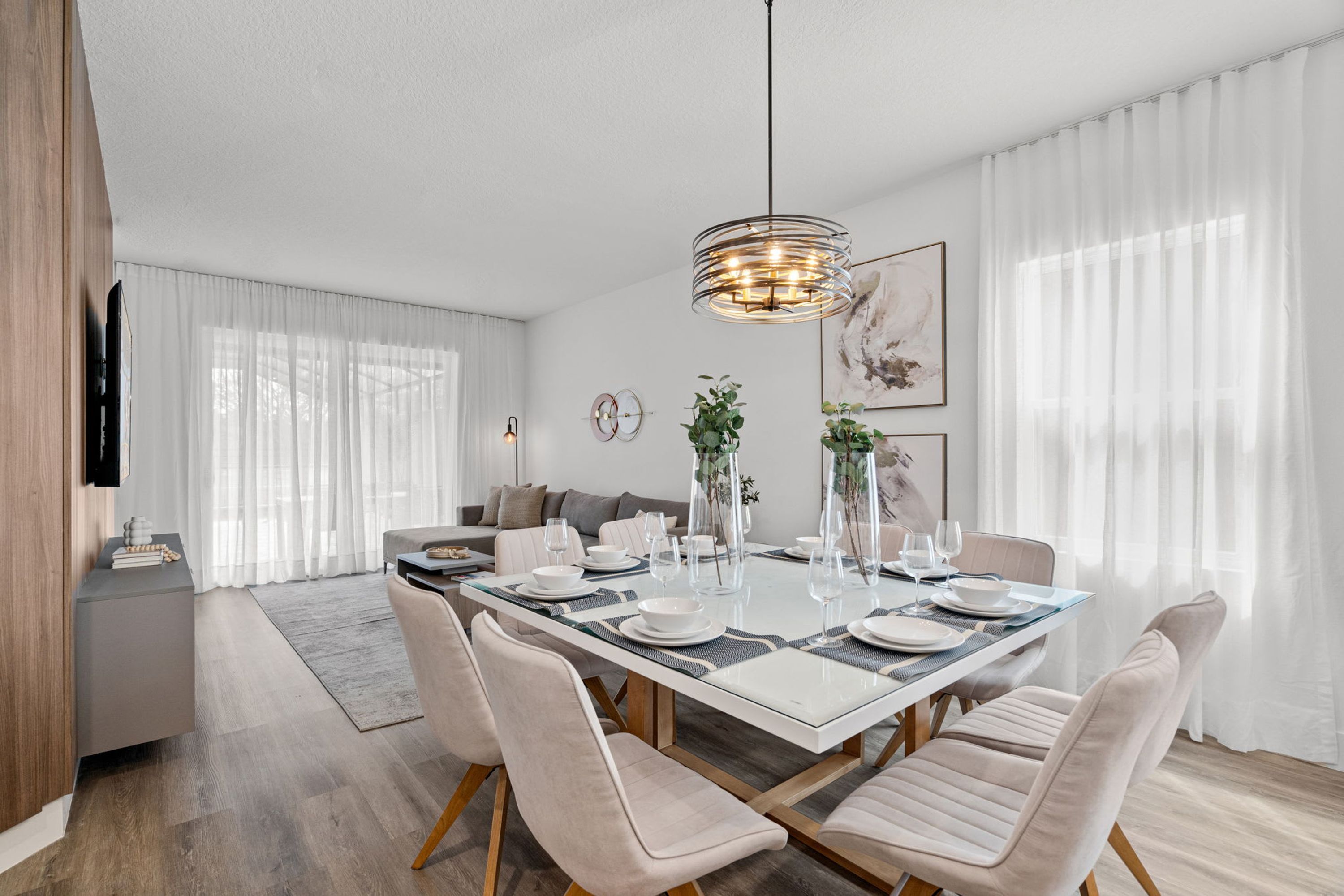 Un comedor moderno con una mesa de vidrio, sillas tapizadas en beige y una lámpara colgante.