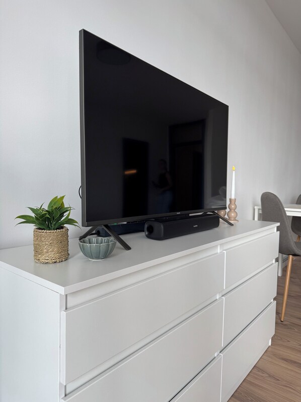 A flat-screen TV on a white dresser with a woven basket, a glass bowl, and a candle.